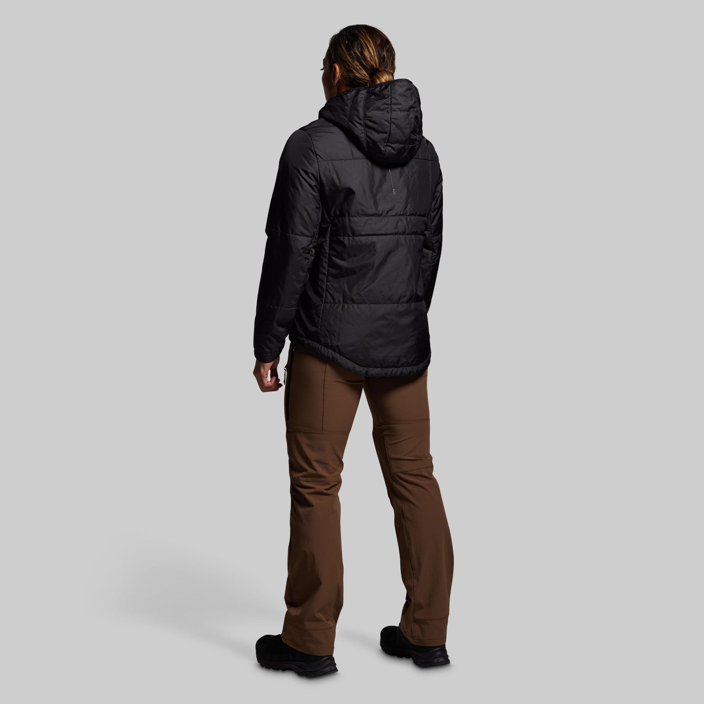 Person wearing a black jacket and brown pants on a gray background