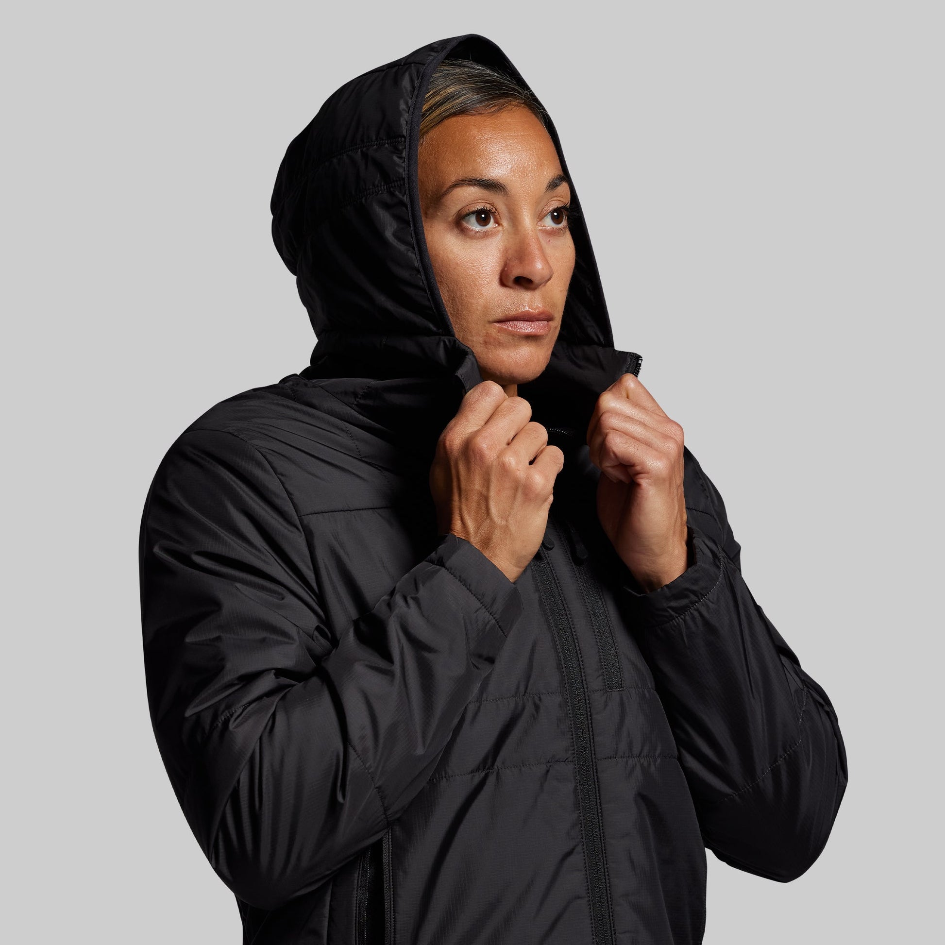 Person wearing a black hooded jacket on a gray background