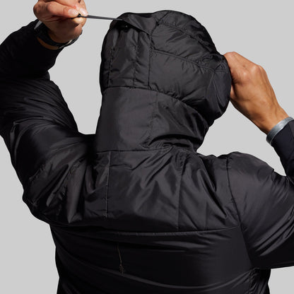 Person wearing a black puffer jacket with a hood against a gray background
