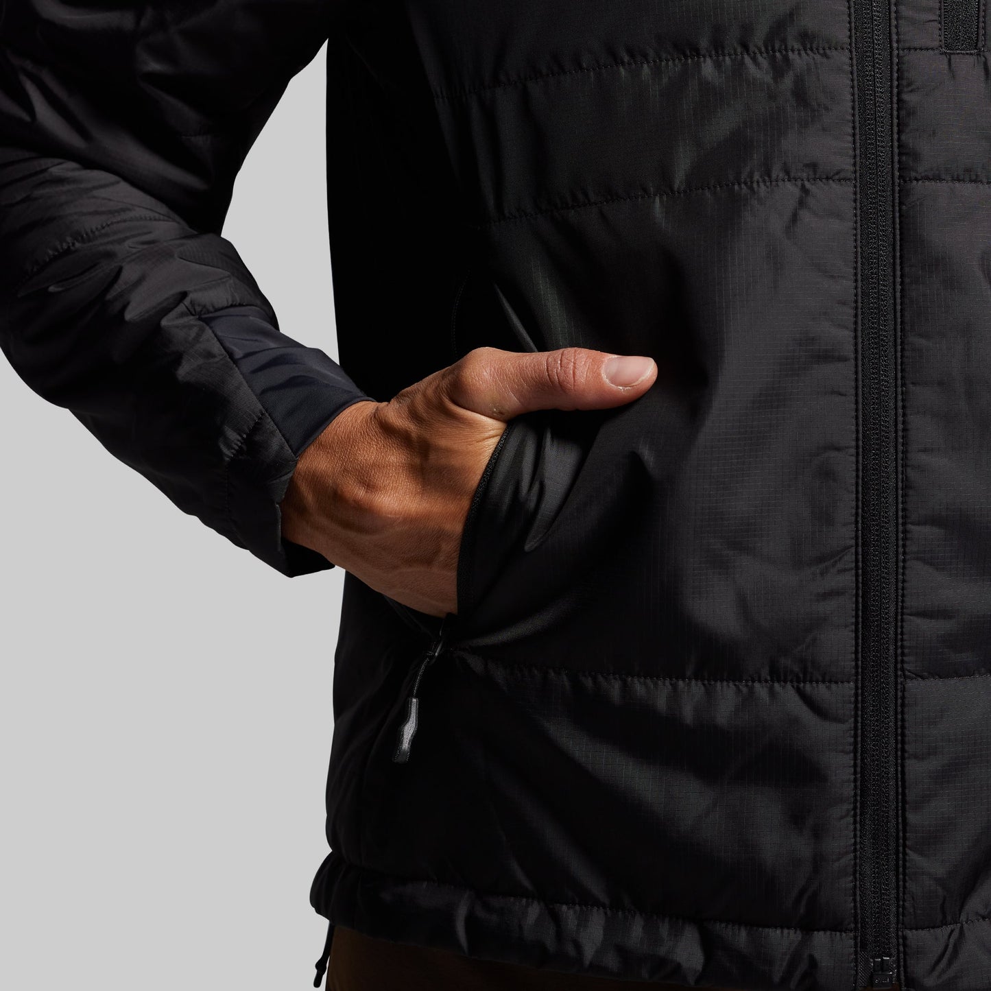 Person wearing a black jacket with a hand in the pocket on a gray background