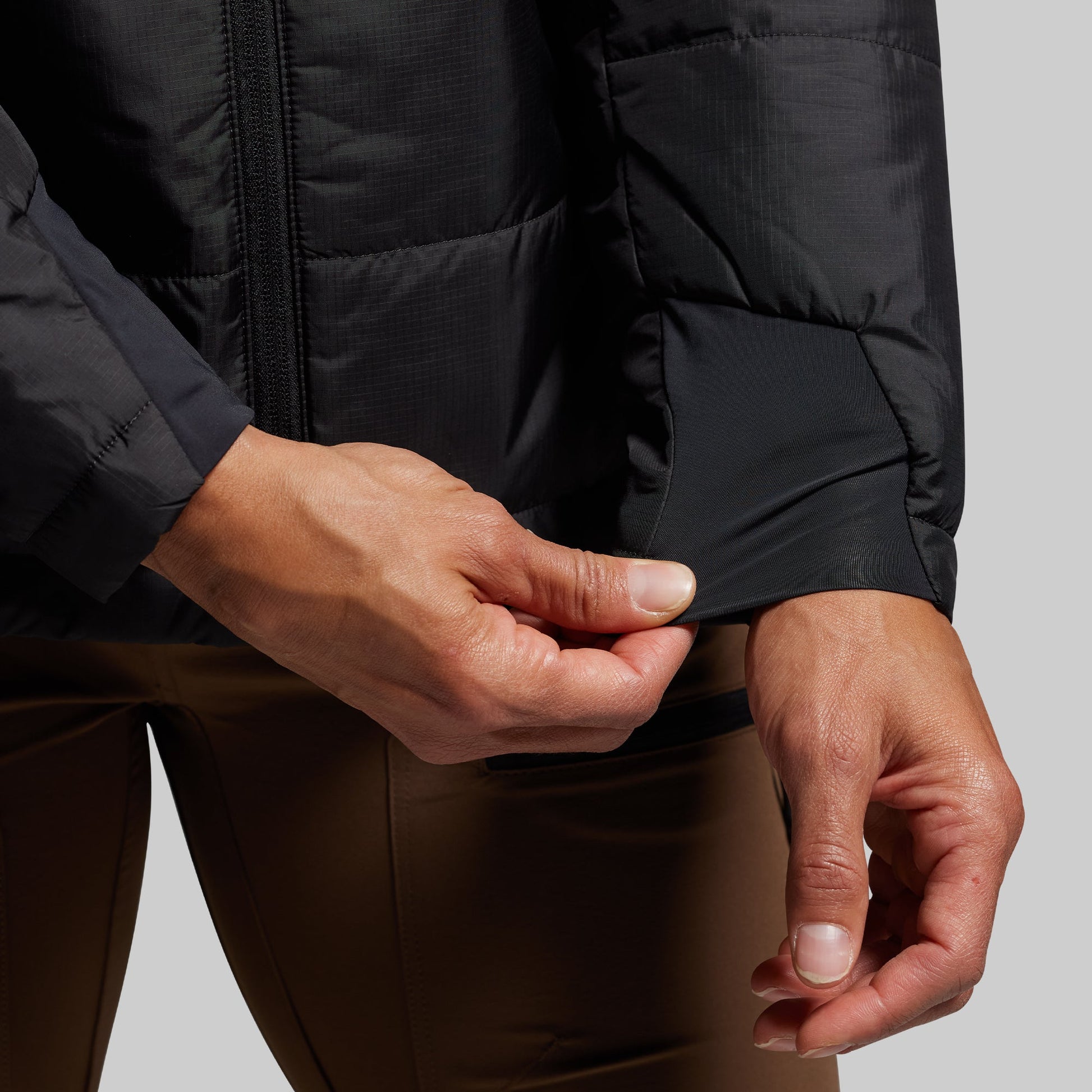 Person wearing a black puffer jacket with hands adjusting the cuffs against a gray background