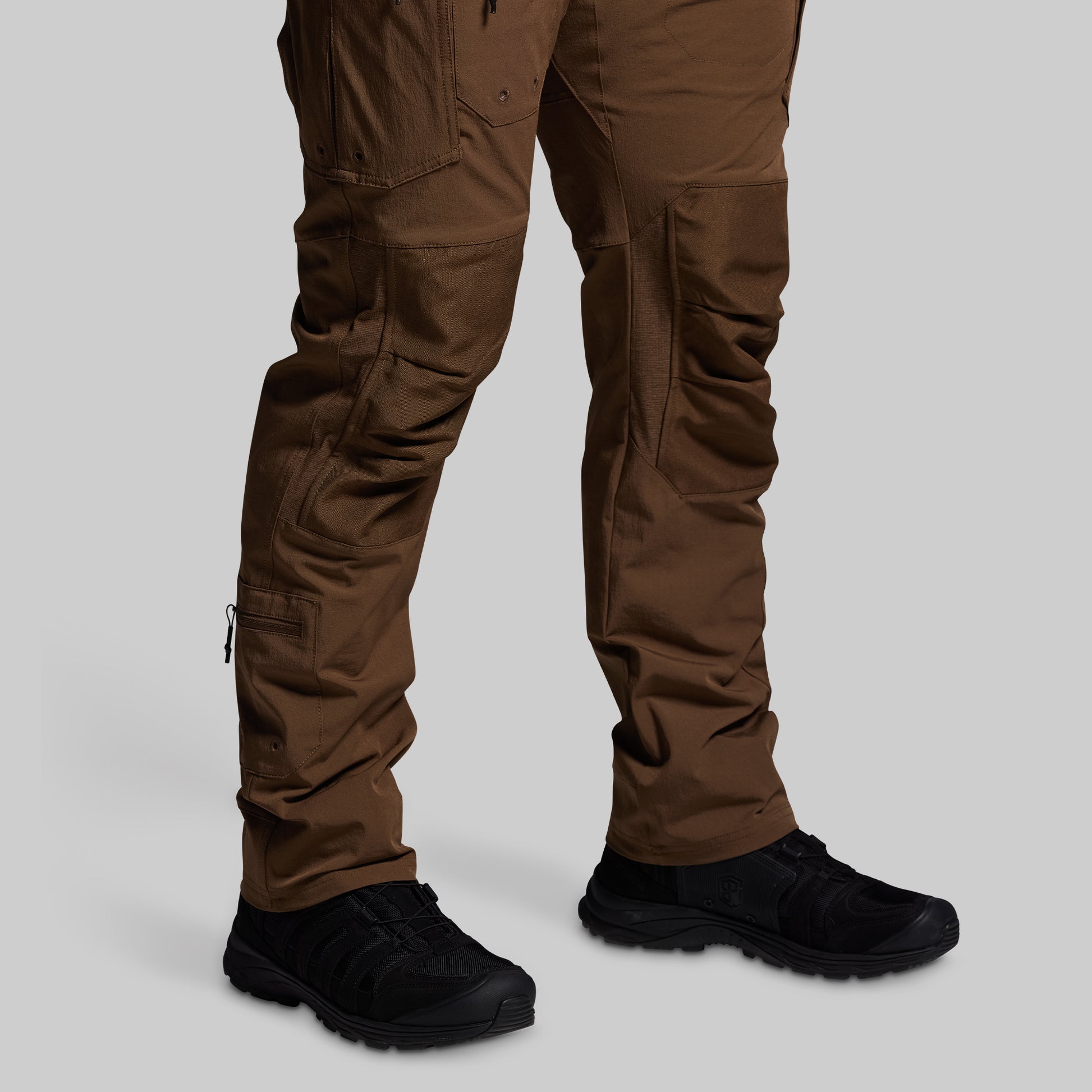 Brown tactical pants with black shoes on a light gray background