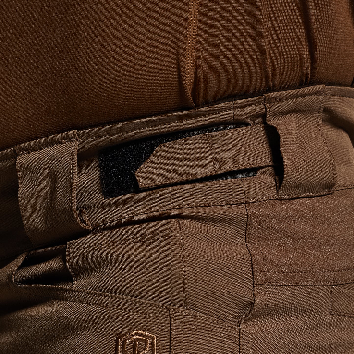 Close-up of brown tactical pants with a visible brand logo.