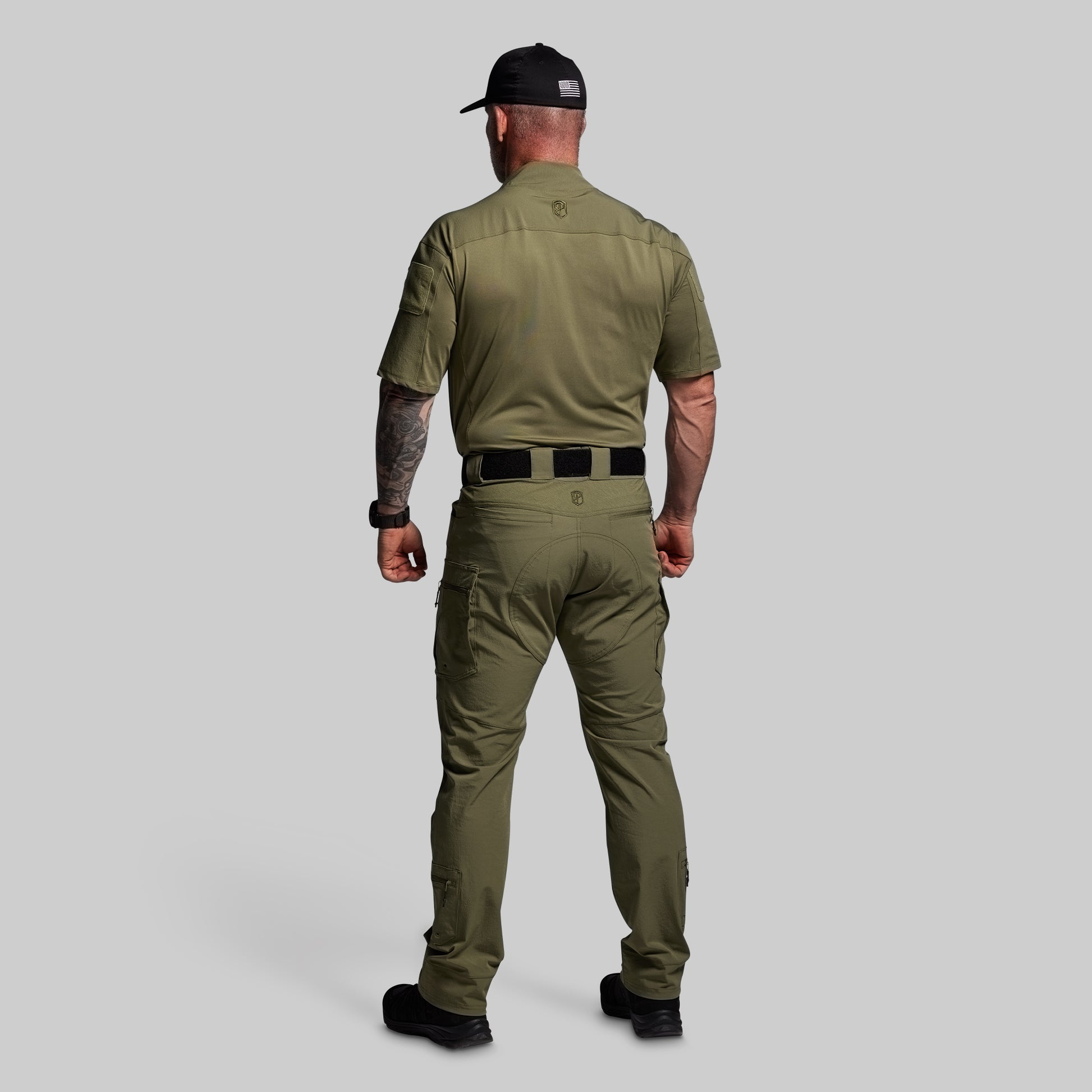 Man wearing a green shirt and pants with a black cap on a gray background