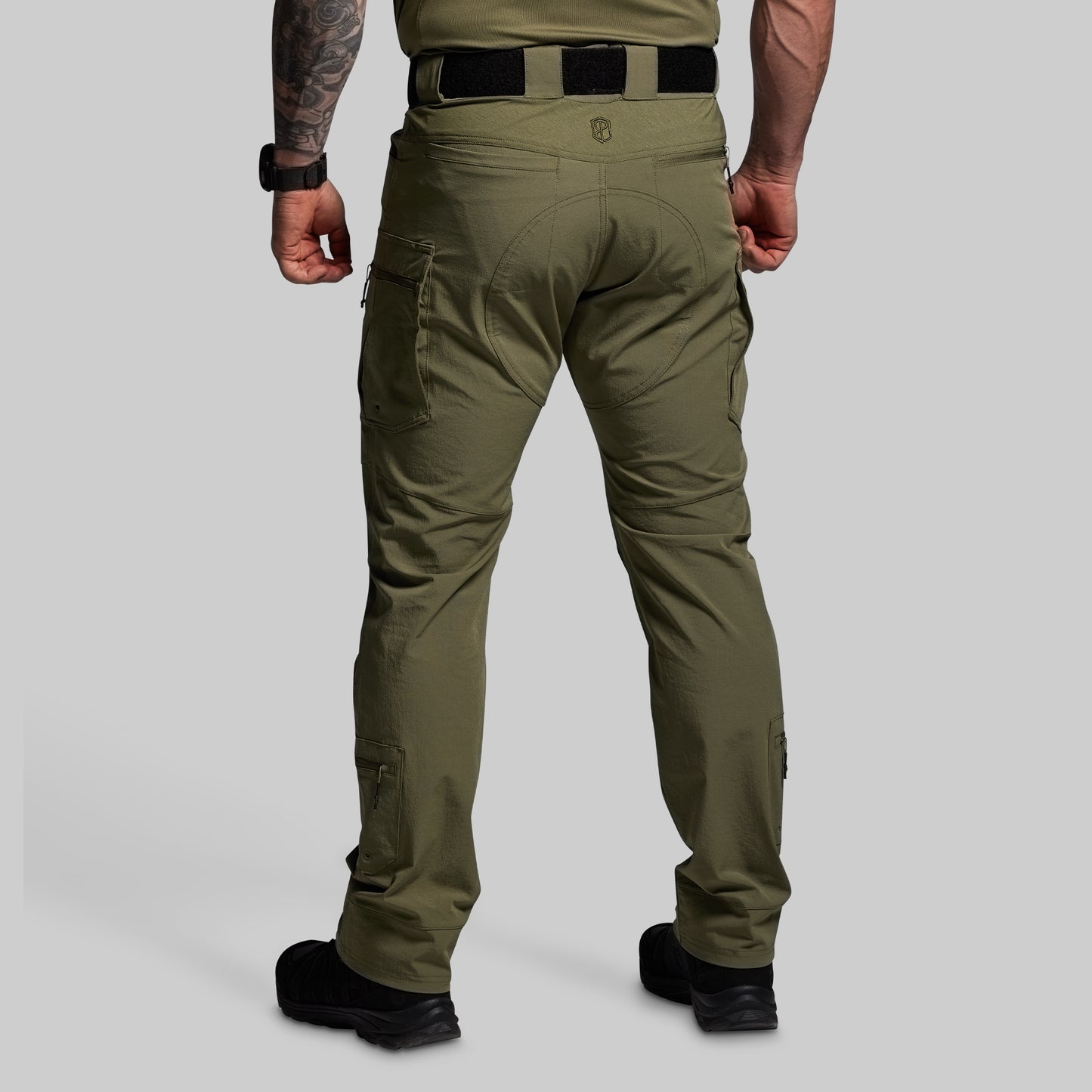 Person wearing olive green tactical pants on a gray background