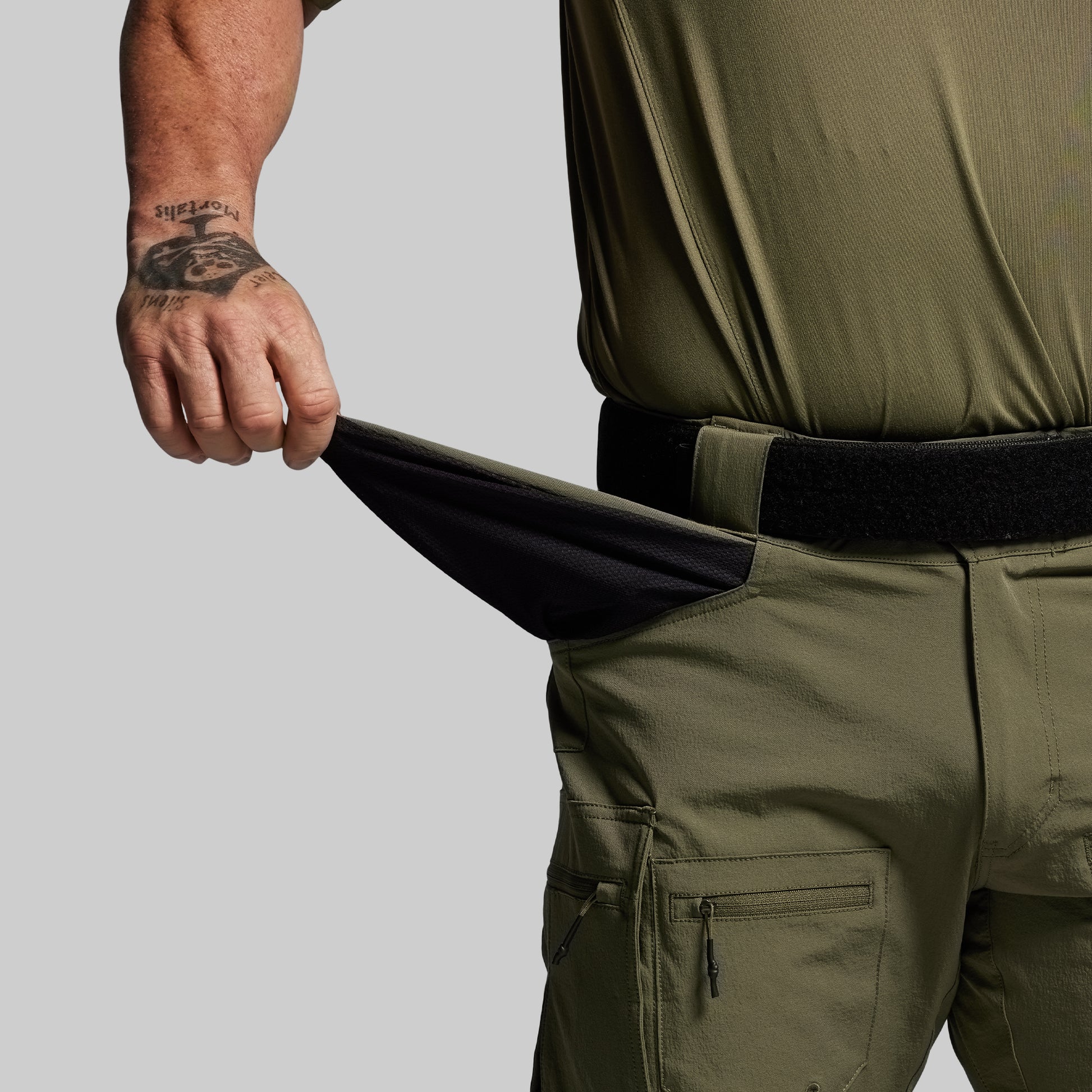 Person wearing olive green pants with a black belt on a gray background