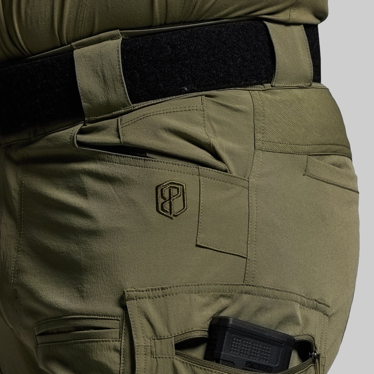 Olive green tactical pants with a logo on a gray background
