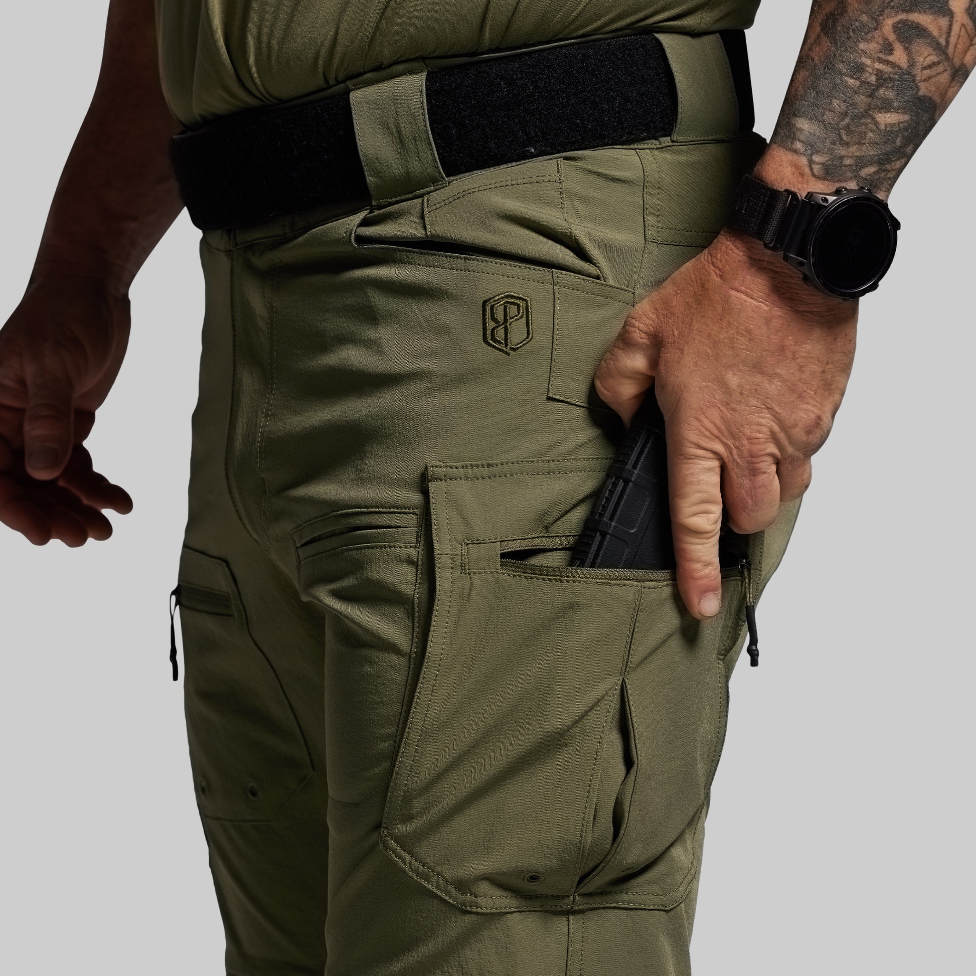 Person wearing green tactical pants with a visible brand logo on a gray background