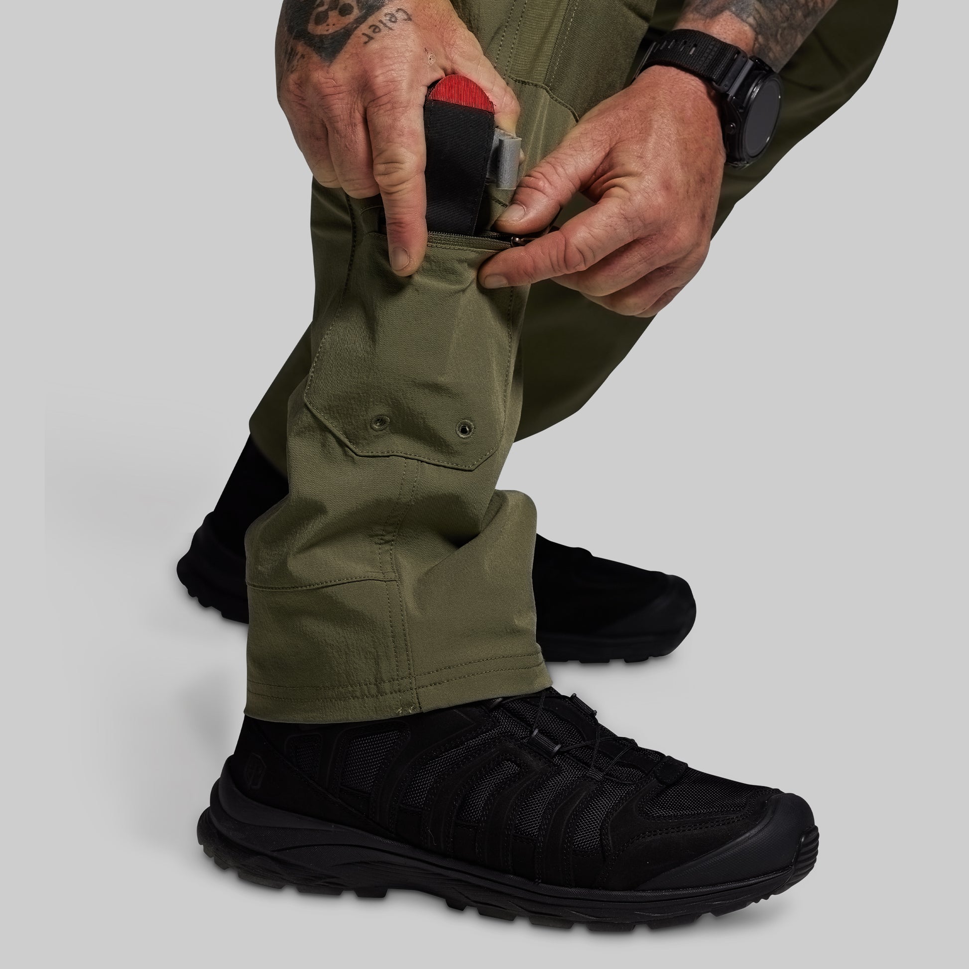 Person wearing green pants and black shoes with a gray background
