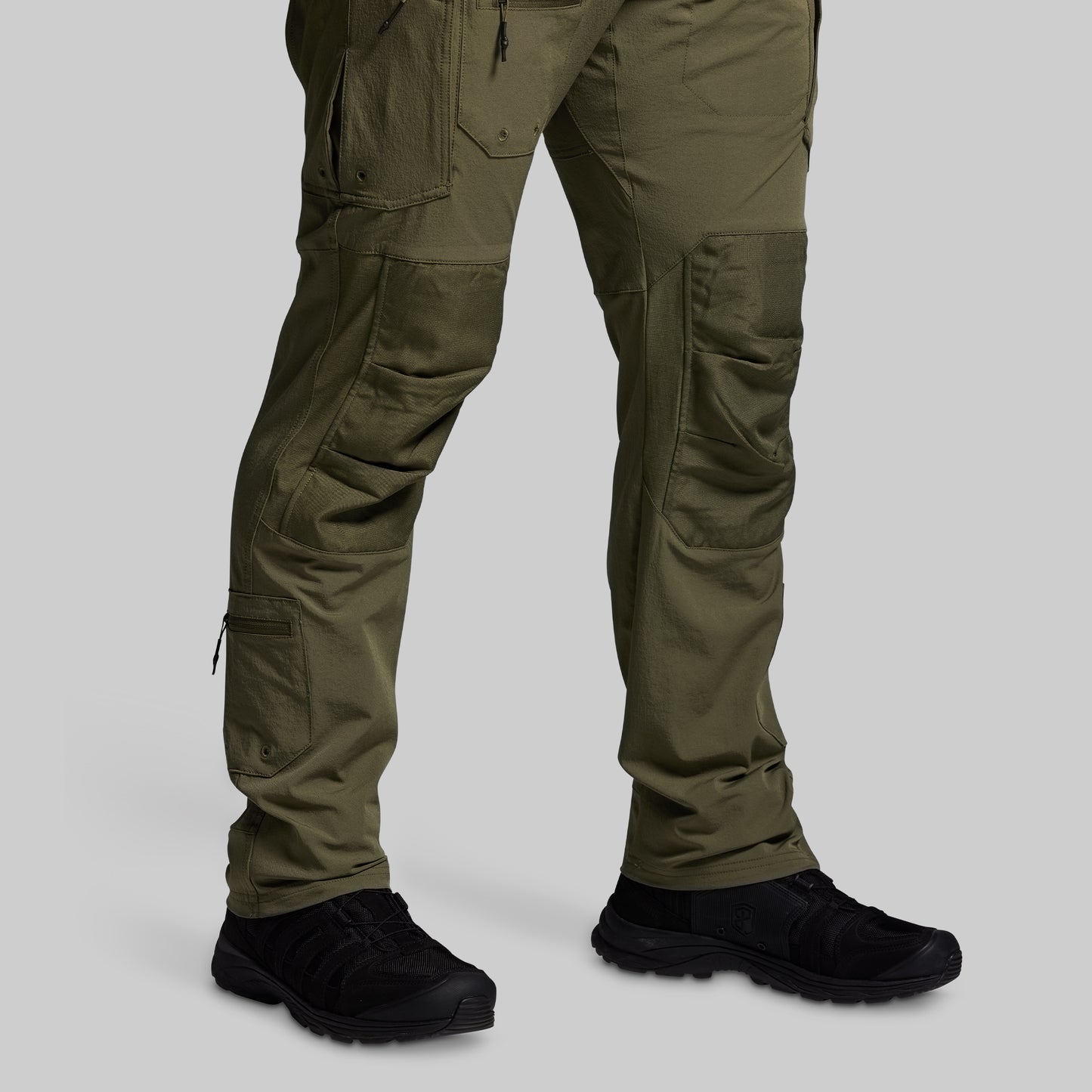 Olive green tactical pants with black shoes on a light gray background