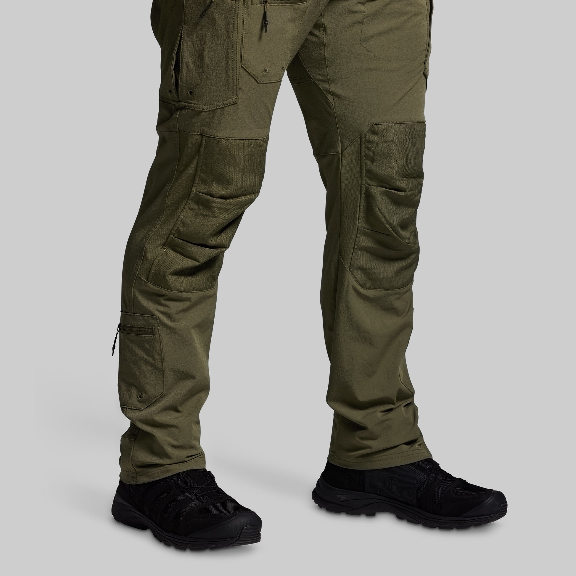 Olive green tactical pants with black shoes on a light gray background