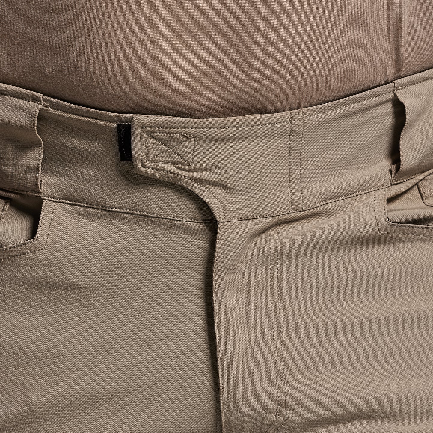 Close-up of beige pants with a brand logo on the waistband.
