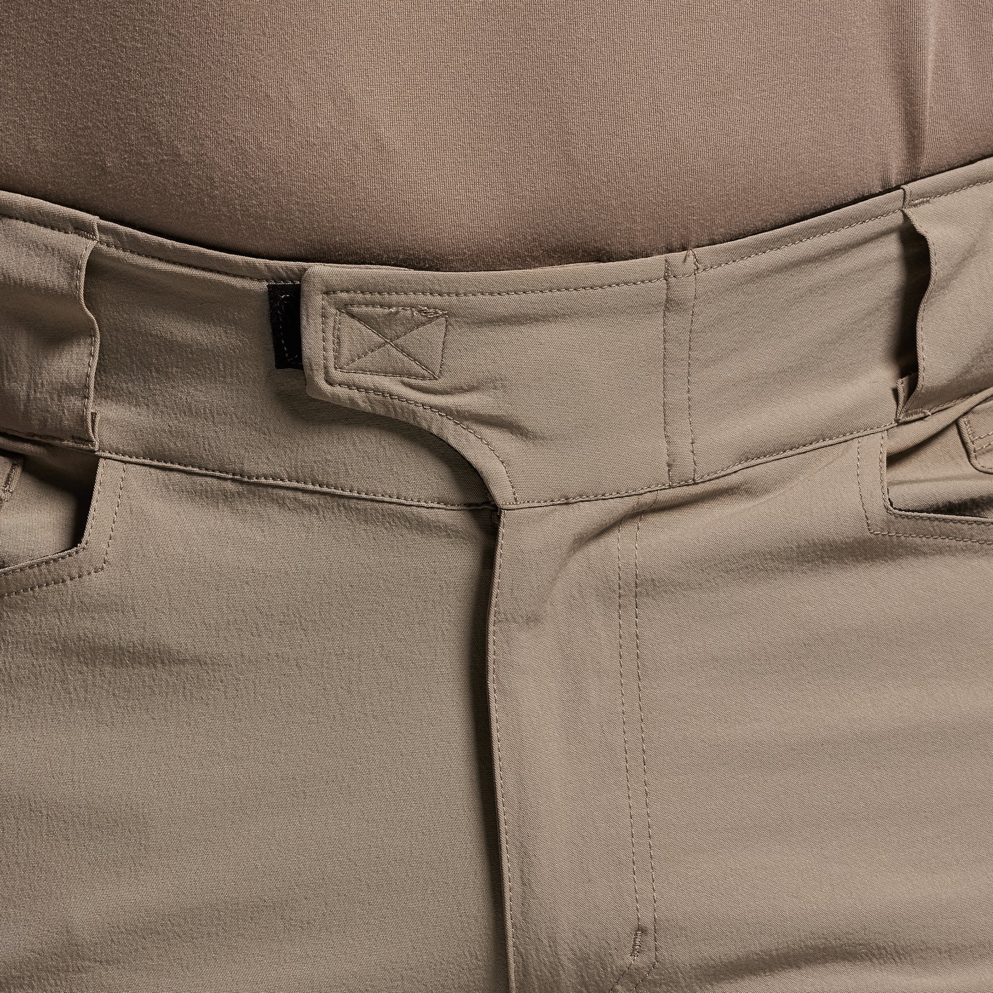 Close-up of beige pants with a brand logo on the waistband.