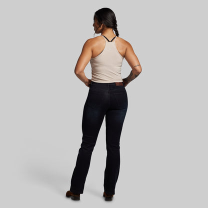 Woman wearing a beige tank top and dark jeans on a gray background
