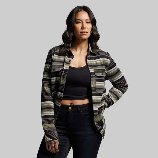 Woman wearing a patterned shirt over a black top and jeans on a gray background