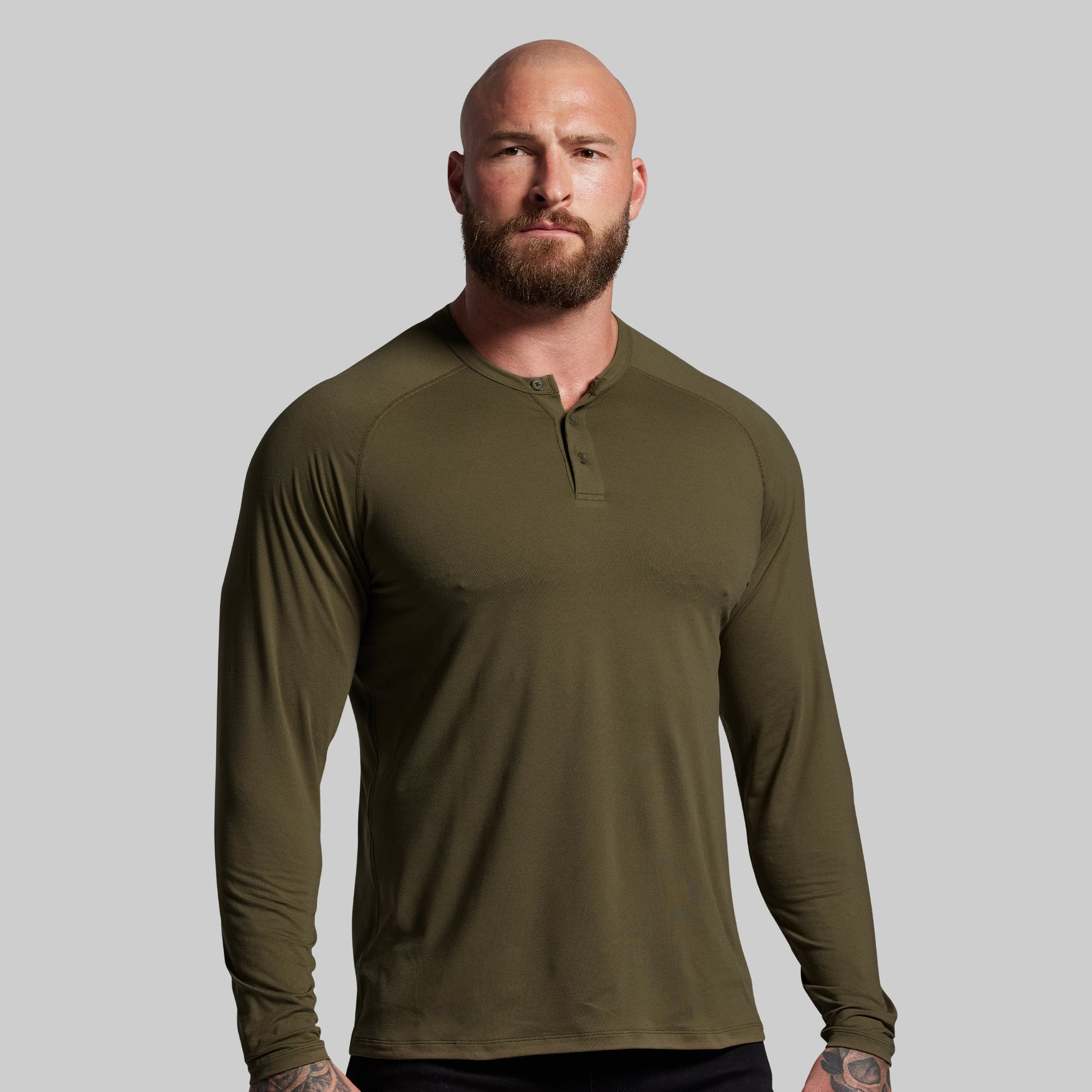Man wearing an olive green long-sleeve shirt against a gray background