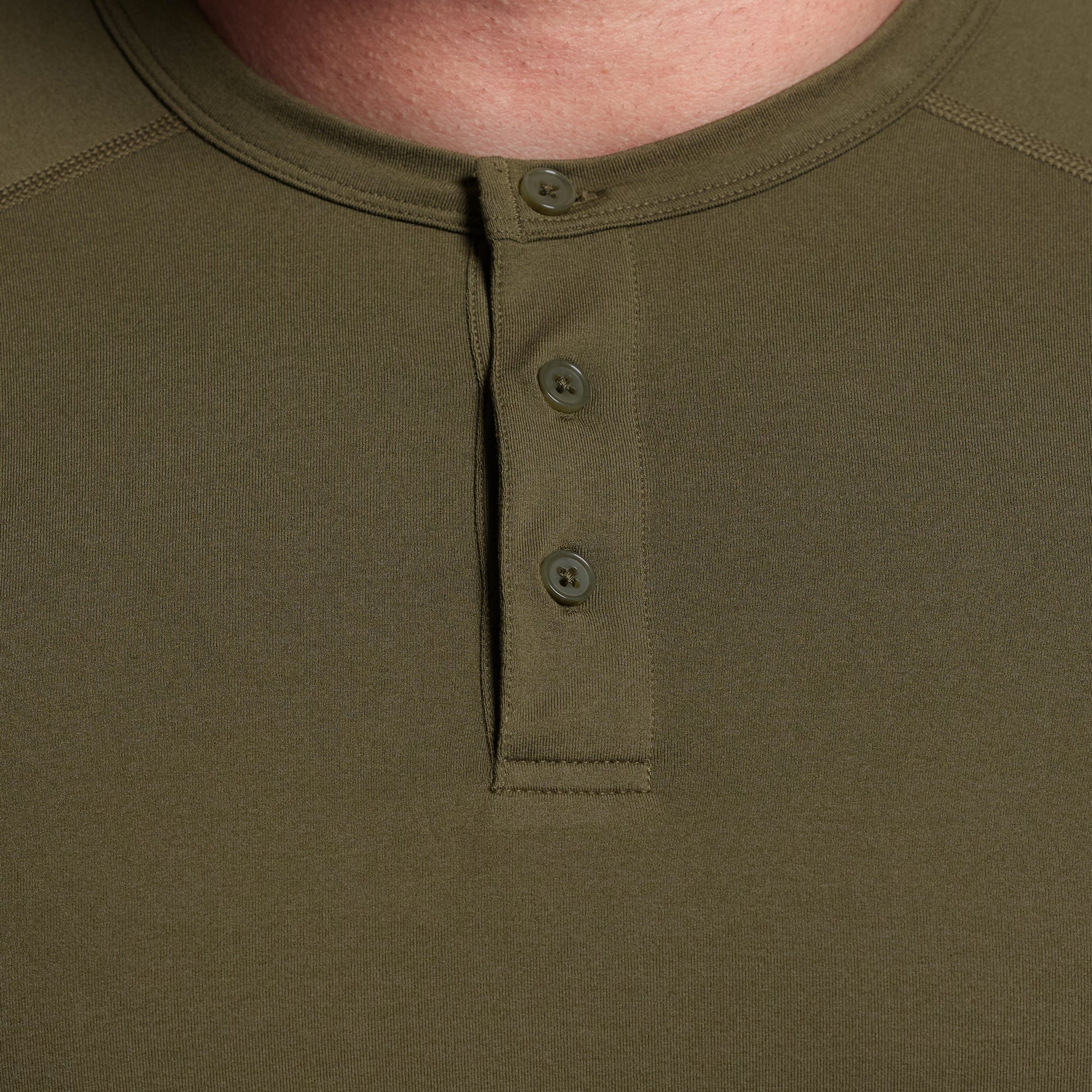 Close-up of a green henley shirt with buttons on a plain background