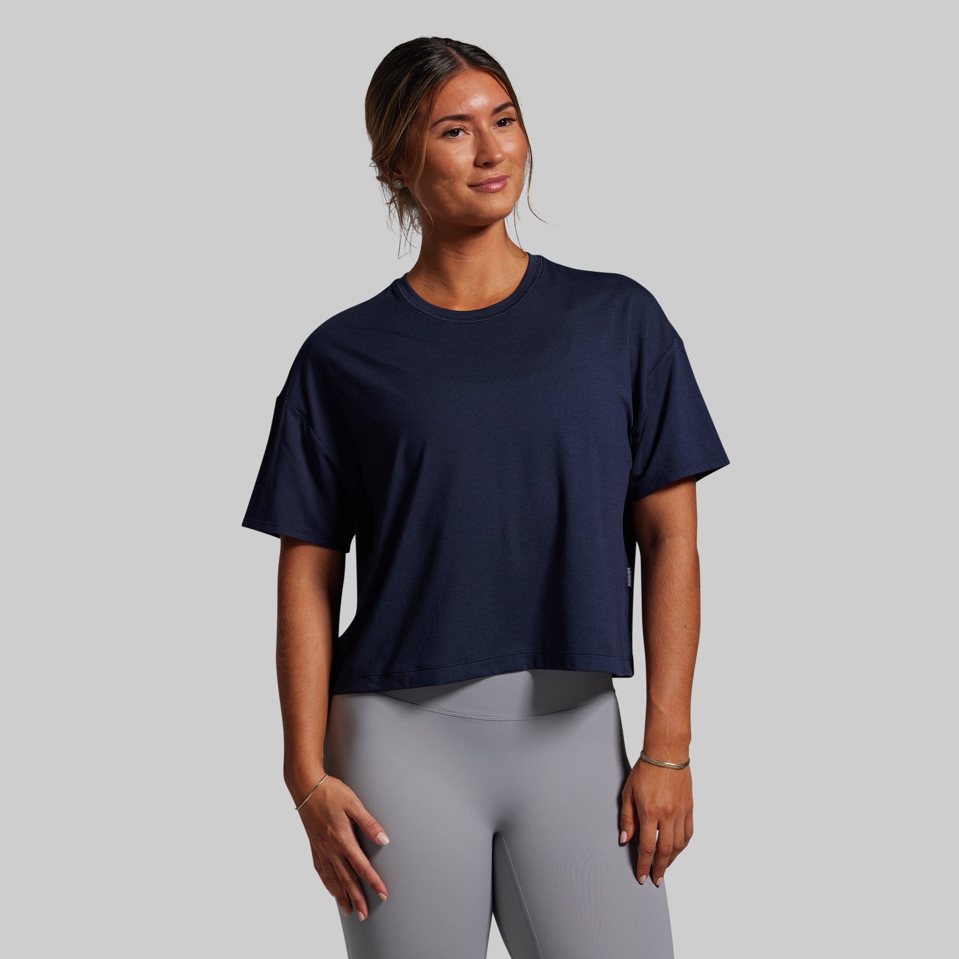 Woman wearing a navy blue t-shirt and gray leggings against a plain background