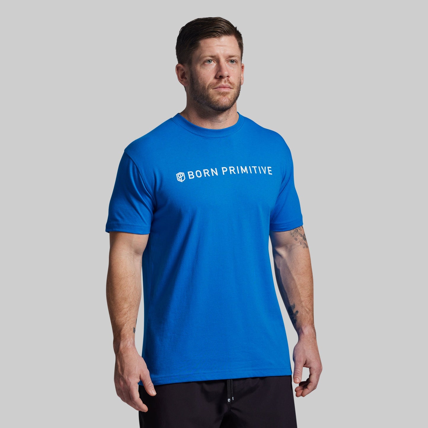 Man wearing a blue 'Born Primitive' t-shirt on a gray background