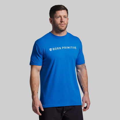 Man wearing a blue 'Born Primitive' t-shirt on a gray background