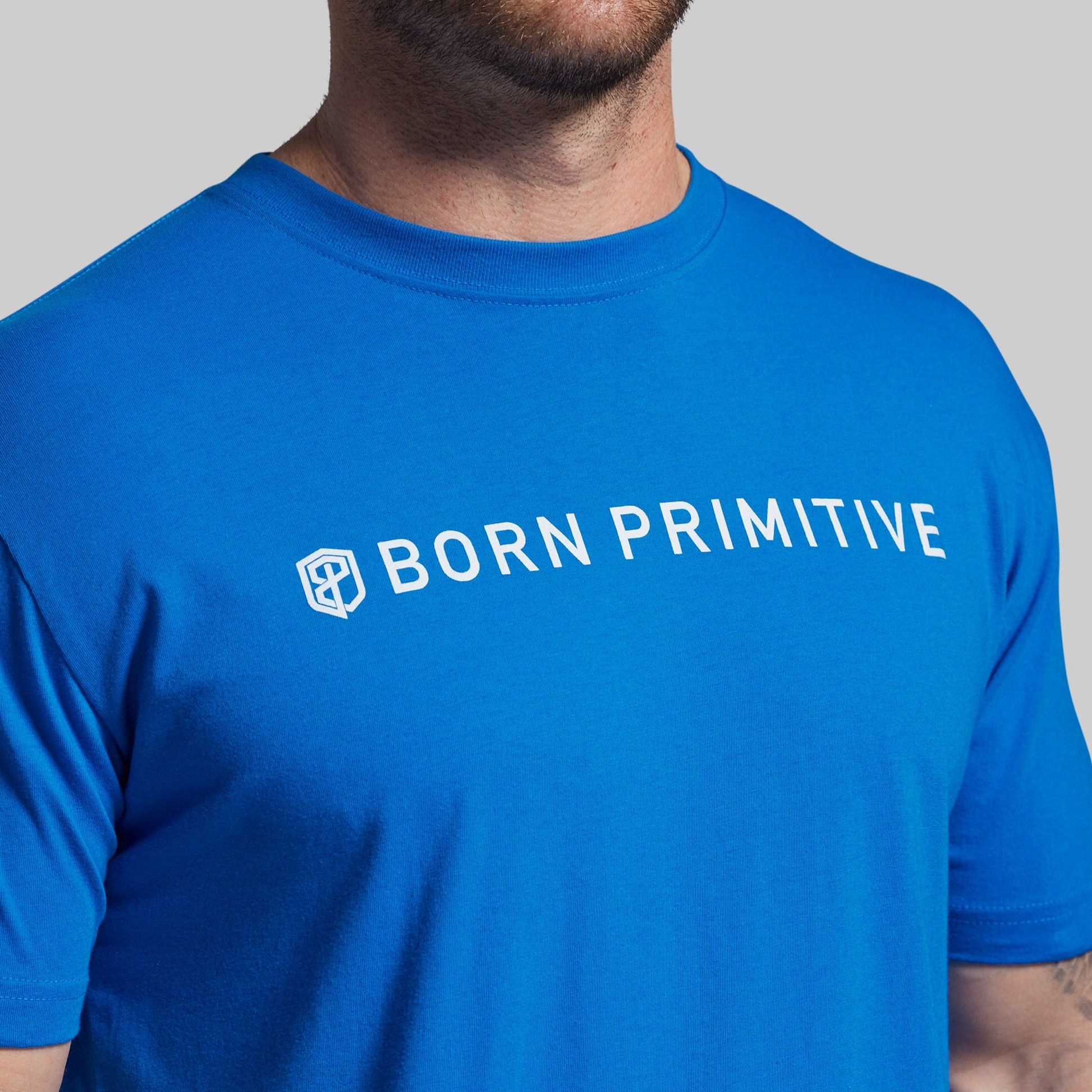 Person wearing a blue t-shirt with 'BORN PRIMITIVE' text and logo.
