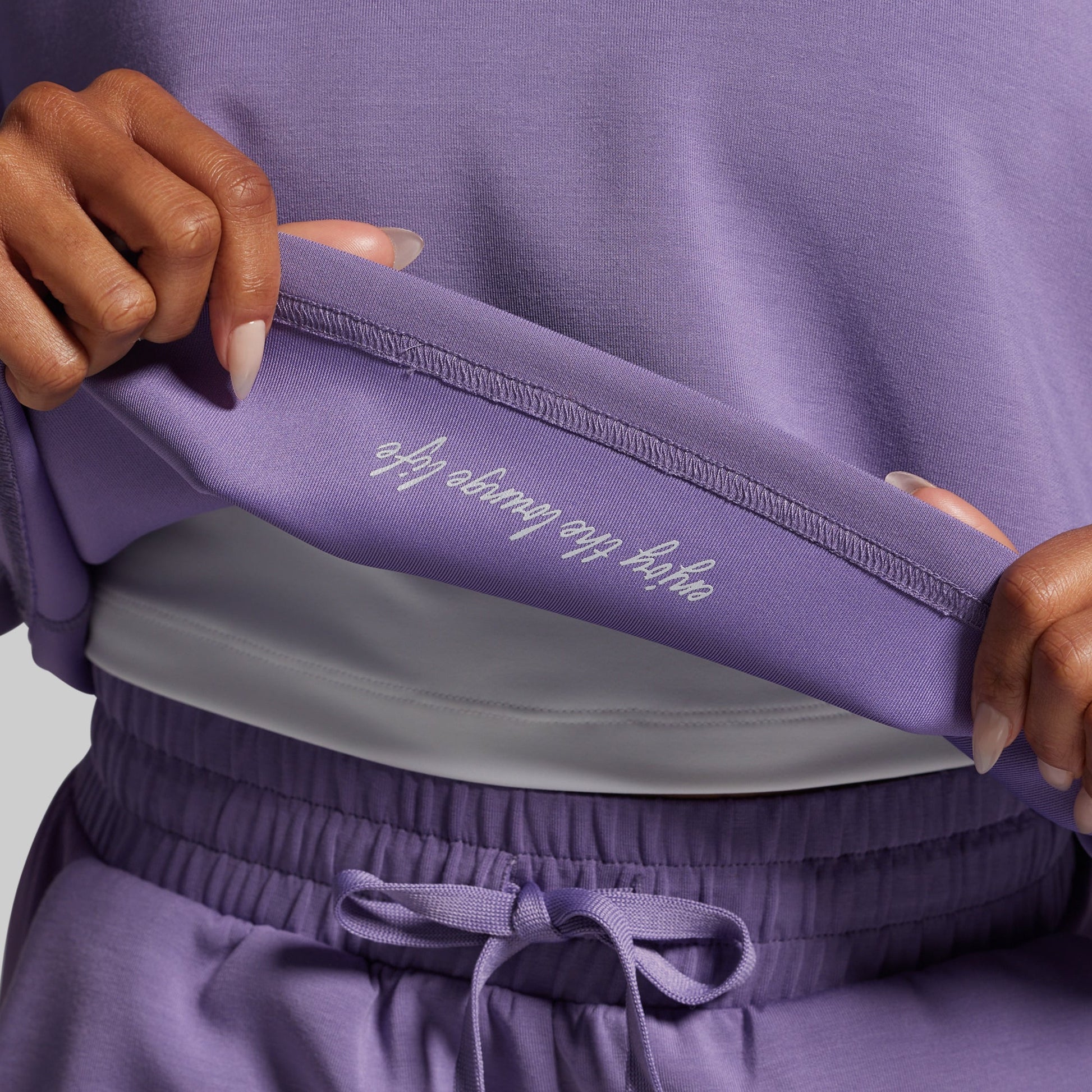 Person wearing a purple outfit with text on the waistband against a neutral background
