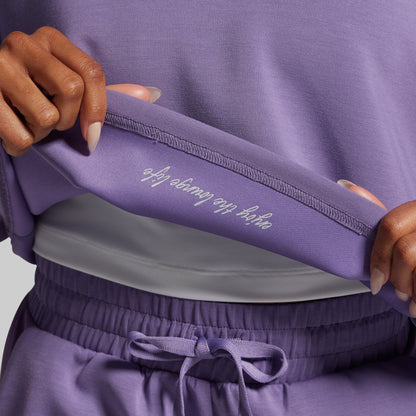 Person wearing a purple outfit with text on the waistband against a neutral background