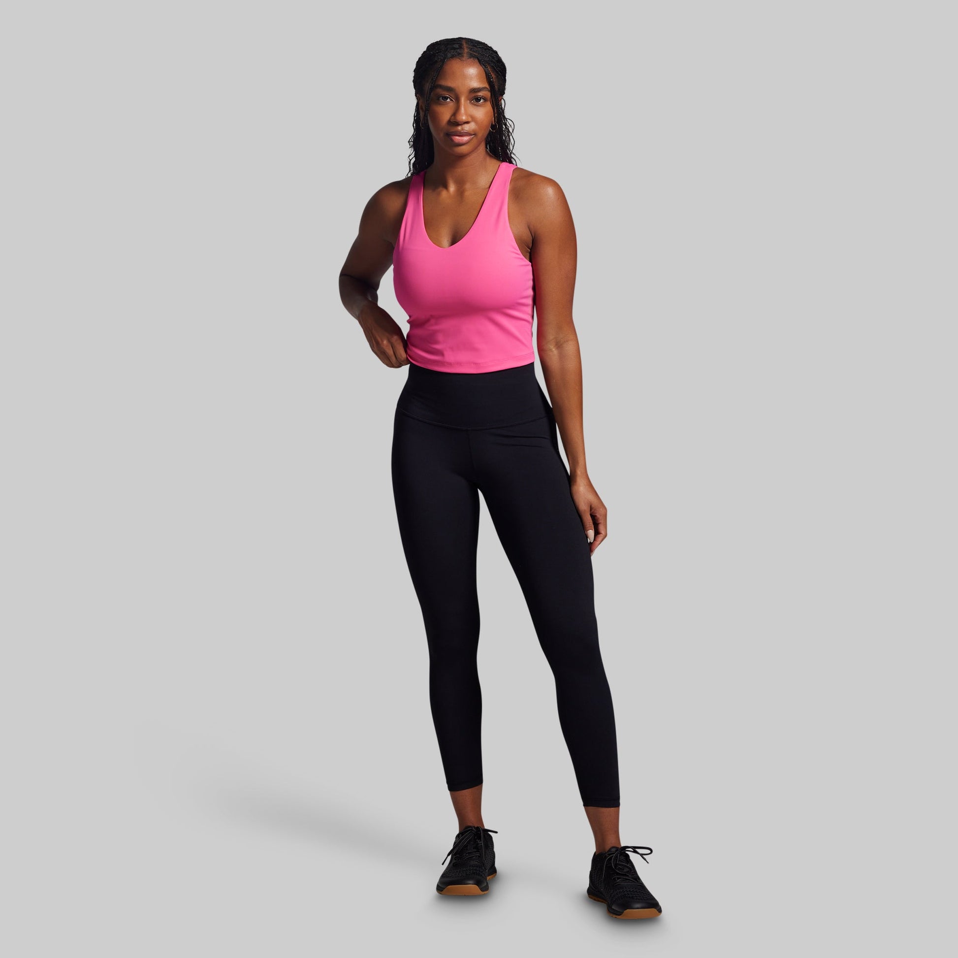 Woman wearing a pink tank top and black leggings on a gray background