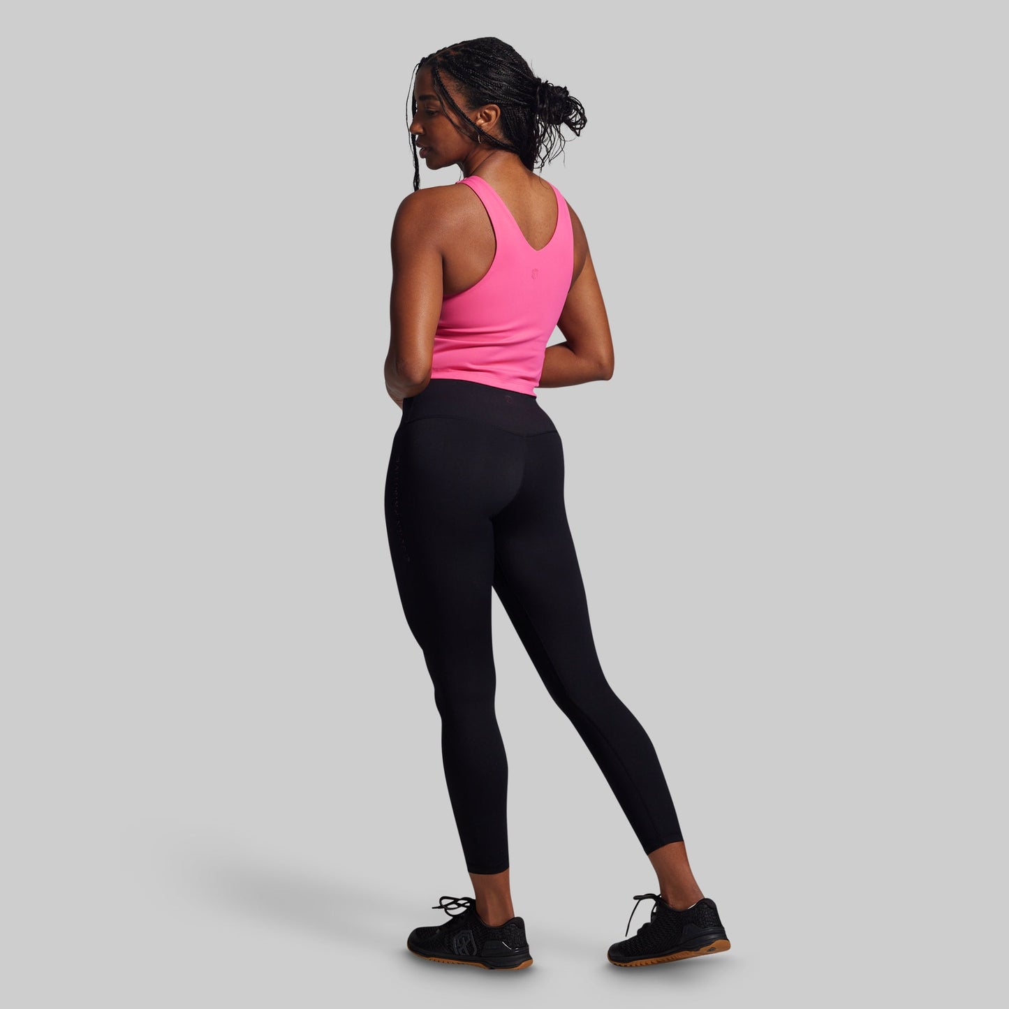Woman wearing a pink tank top and black leggings on a gray background