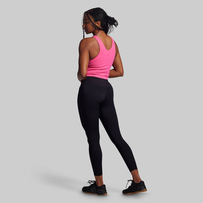 Woman wearing a pink tank top and black leggings on a gray background