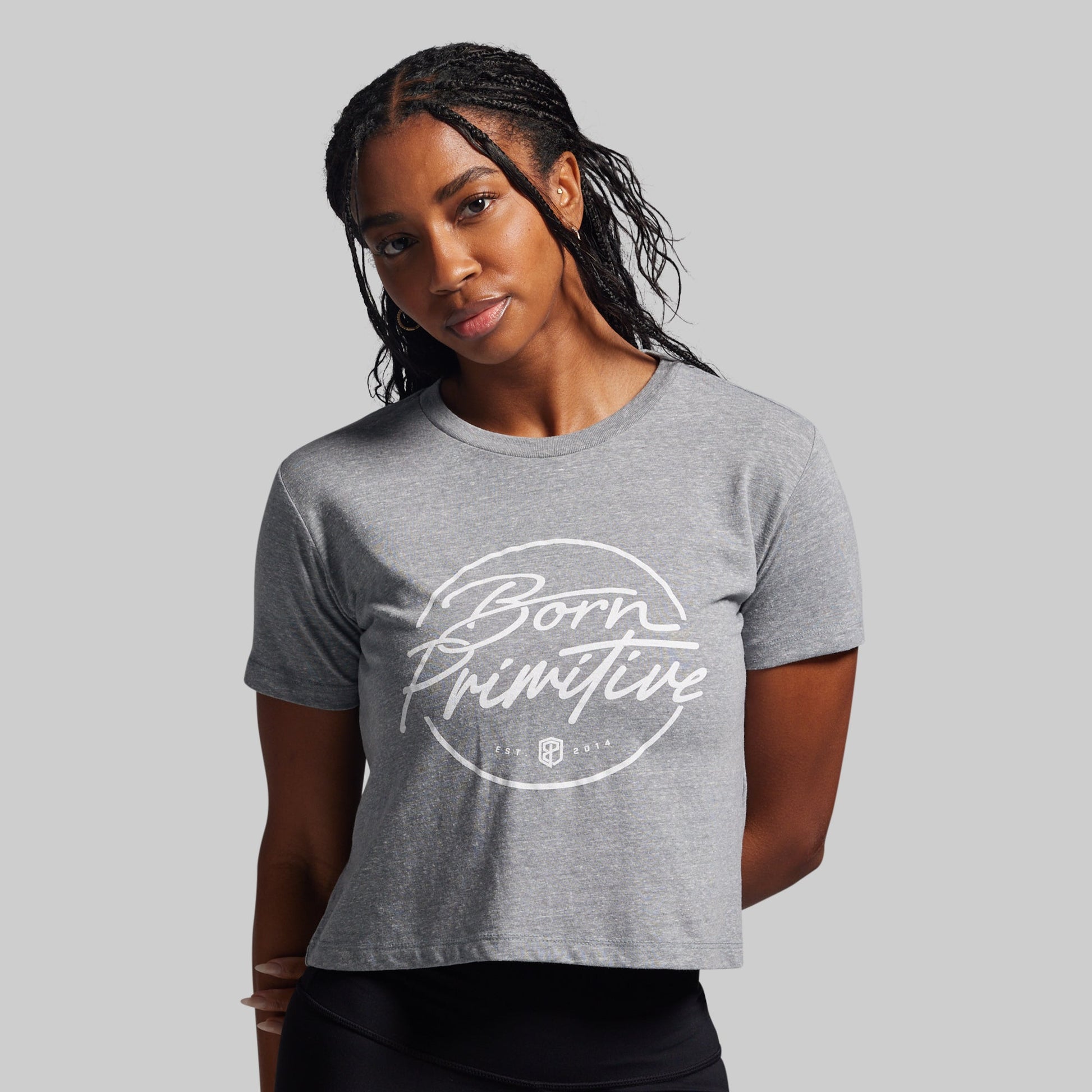 Woman wearing a gray t-shirt with 'Born Primitive' logo on a gray background