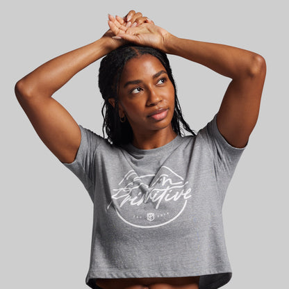 Woman wearing a gray t-shirt with a logo and text on a plain background