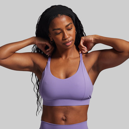 Woman wearing a purple sports bra and leggings against a gray background
