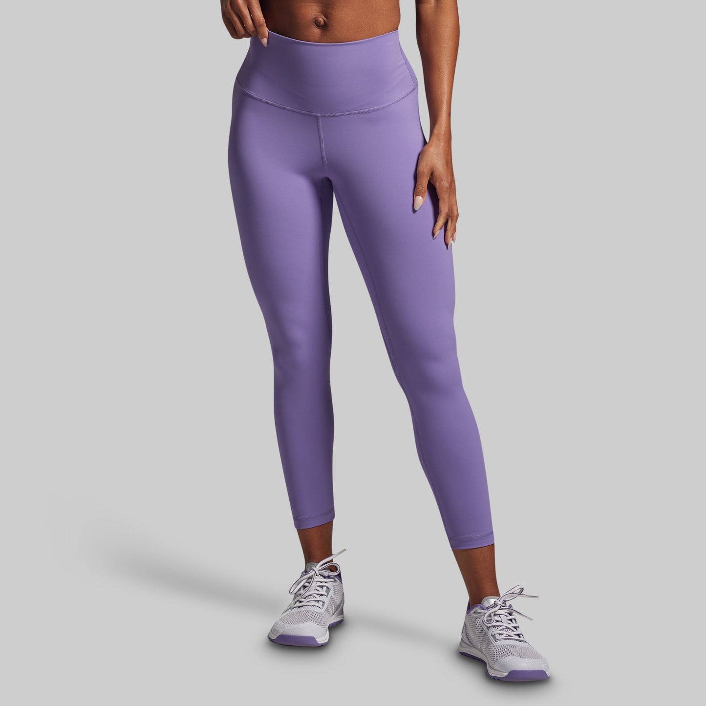 Person wearing purple leggings and white sneakers on a gray background