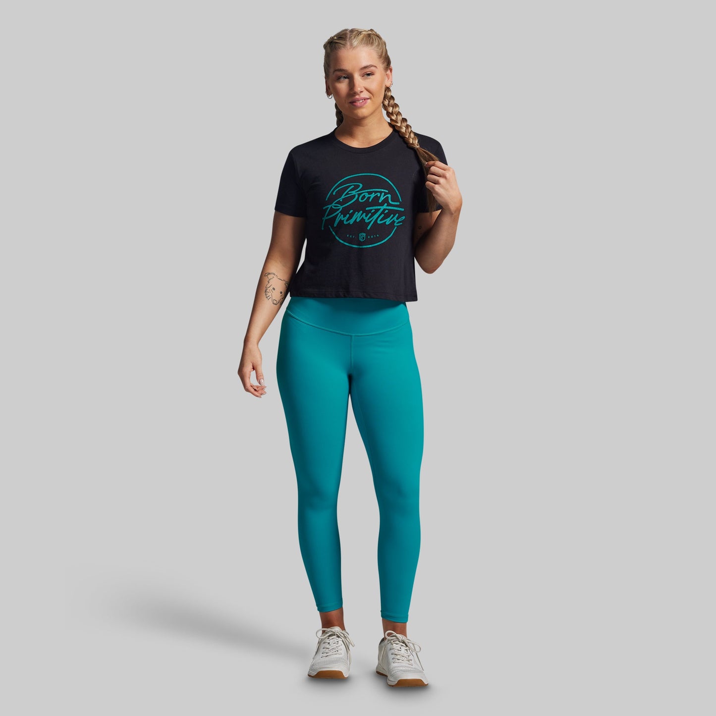 Woman wearing a black t-shirt with green text and teal leggings on a gray background