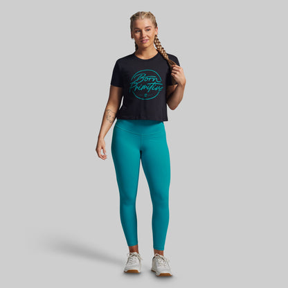 Woman wearing a black t-shirt with green text and teal leggings on a gray background