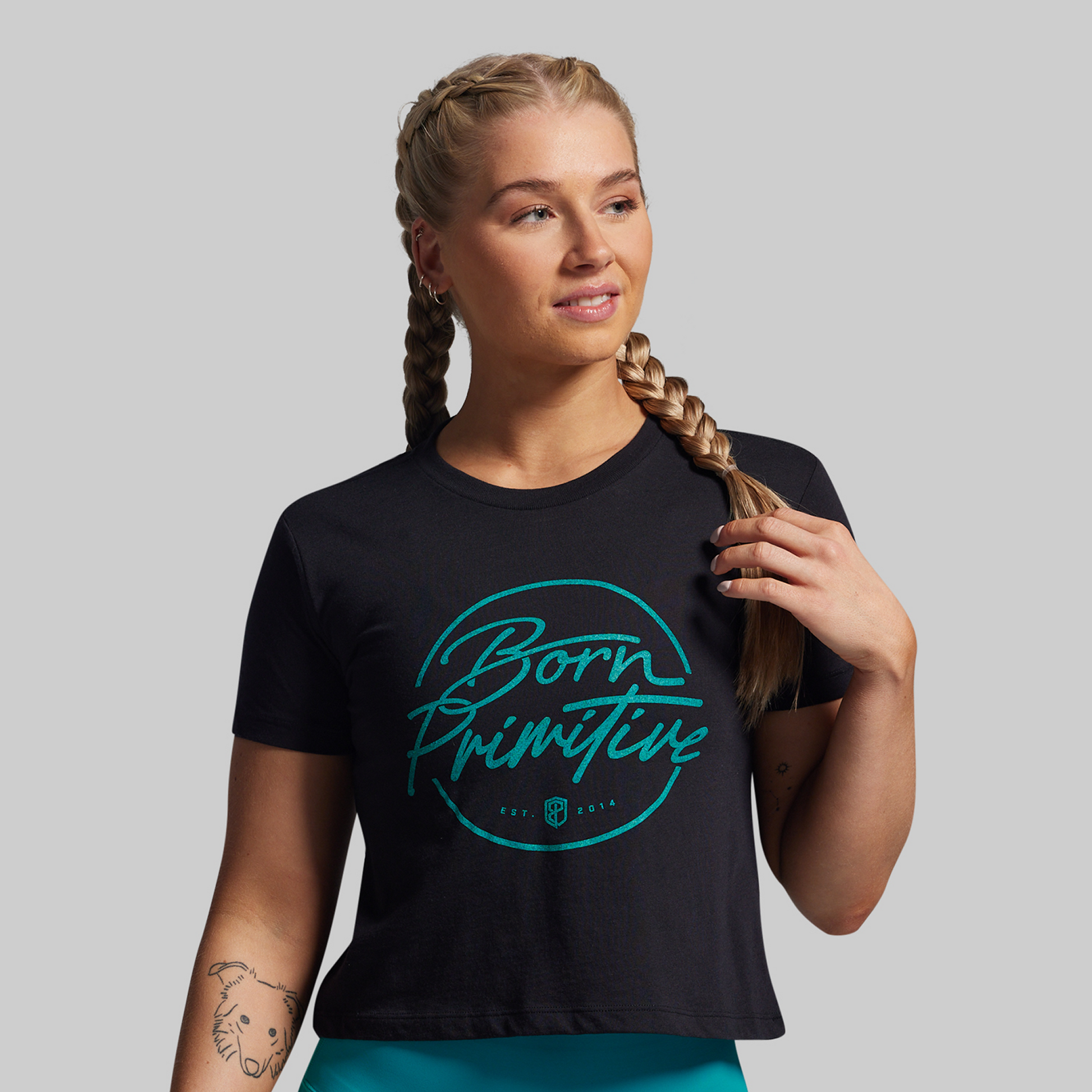 Woman wearing a black t-shirt with 'Born Primitive' logo on a gray background