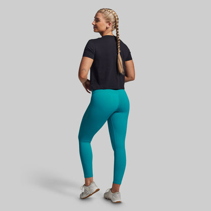 Woman wearing teal leggings and a black top on a gray background