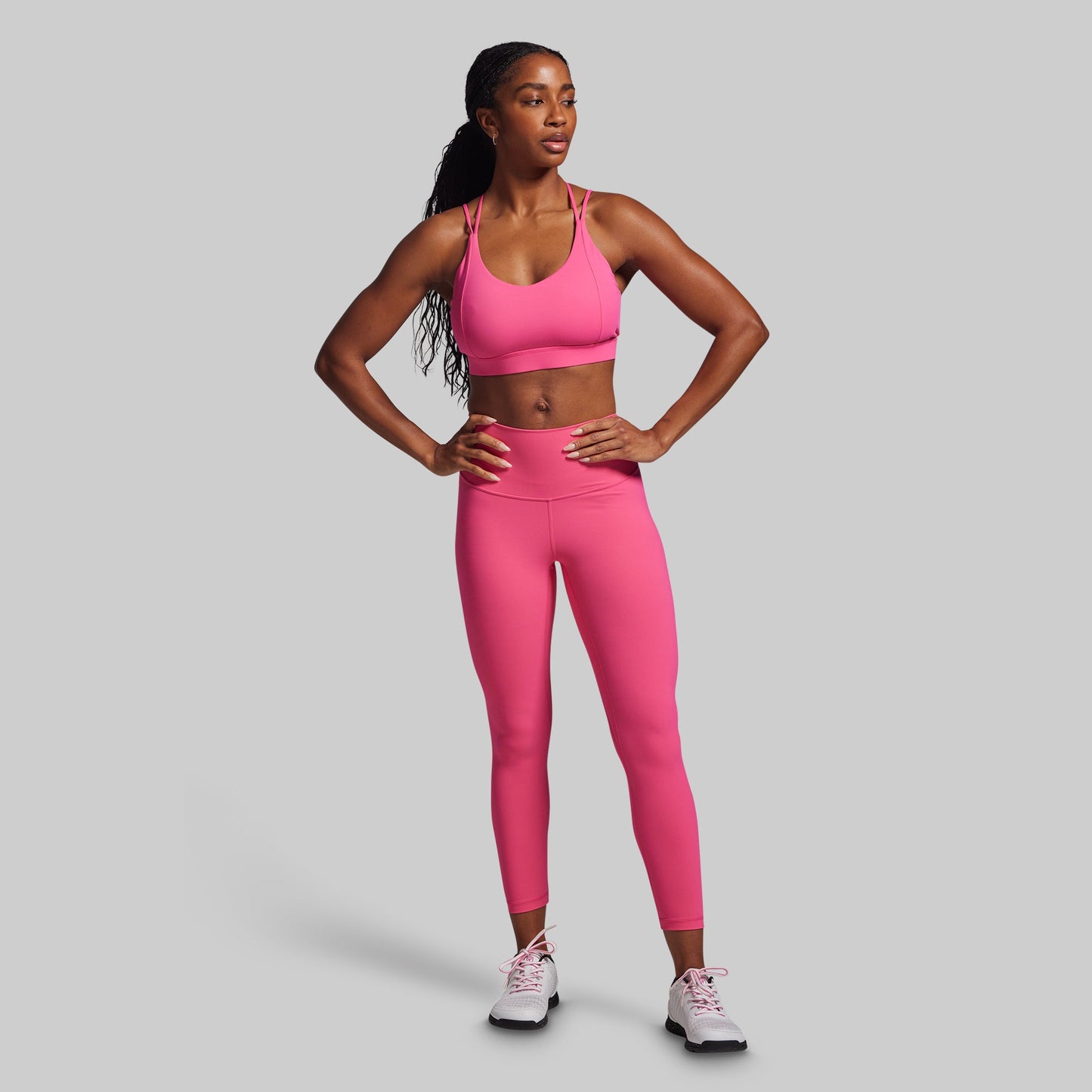 Woman wearing a pink sports bra and leggings set on a gray background