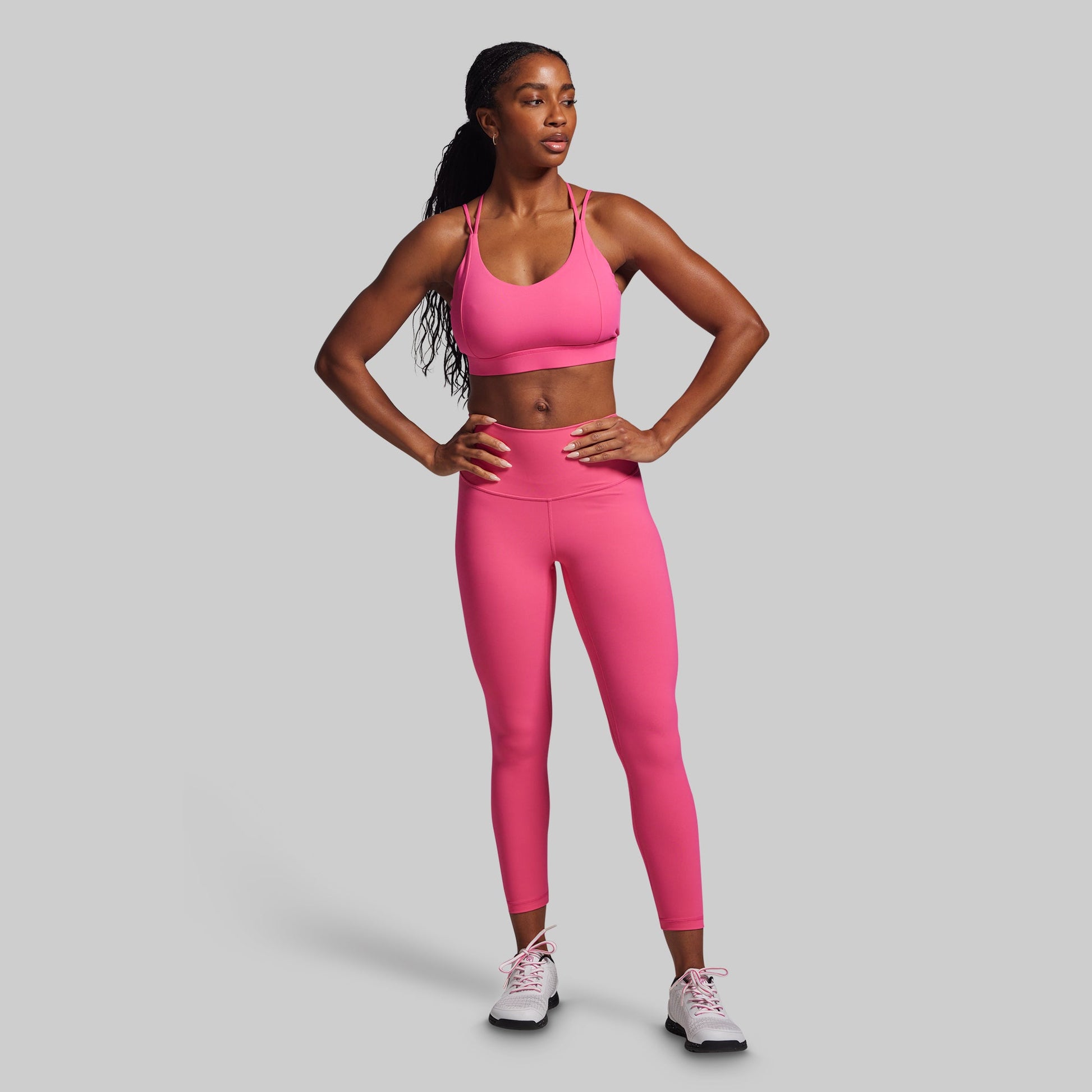 Woman wearing a pink sports bra and leggings set on a gray background