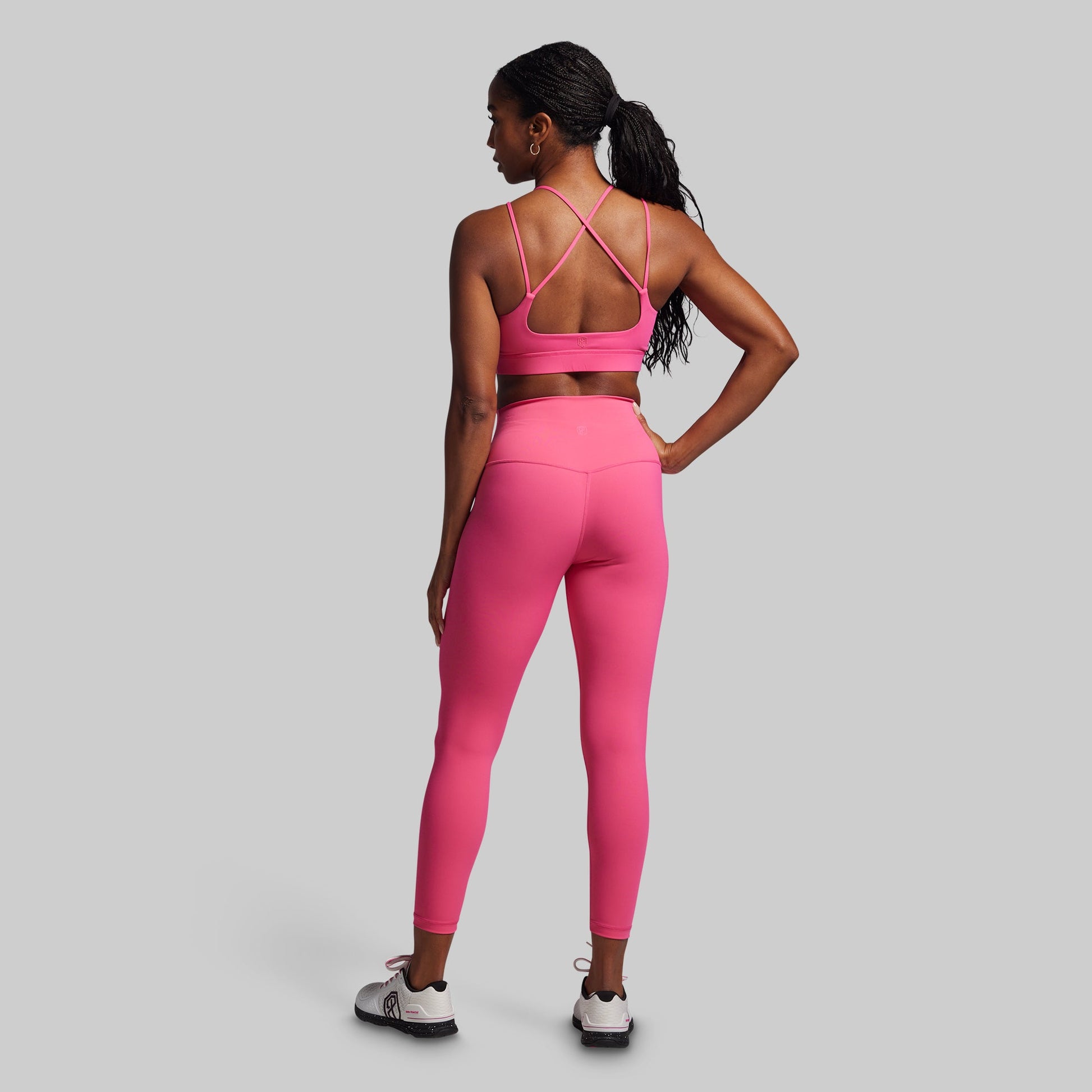 Woman wearing a pink sports bra and leggings set on a gray background