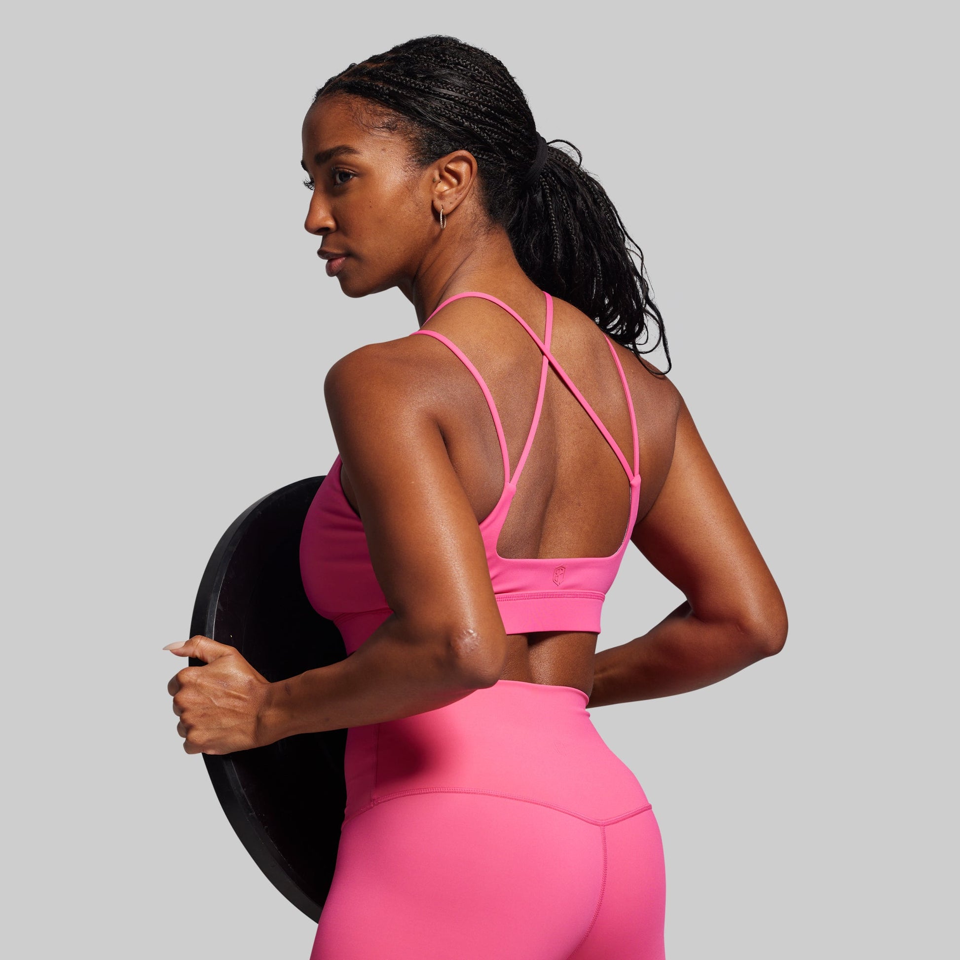 Woman in a pink sports outfit holding a black weight against a gray background
