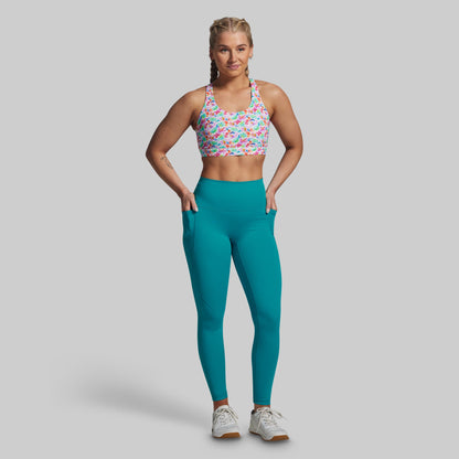 Woman wearing a colorful sports bra and teal leggings on a gray background