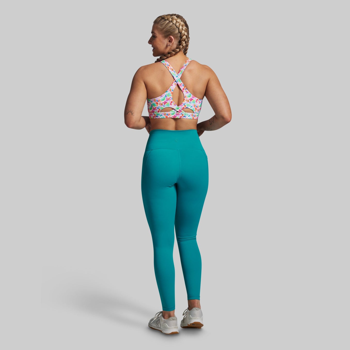 Woman wearing a colorful sports bra and teal leggings on a gray background