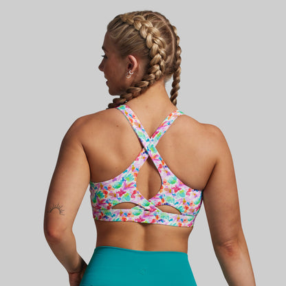 Woman wearing a colorful floral sports bra and teal leggings on a gray background