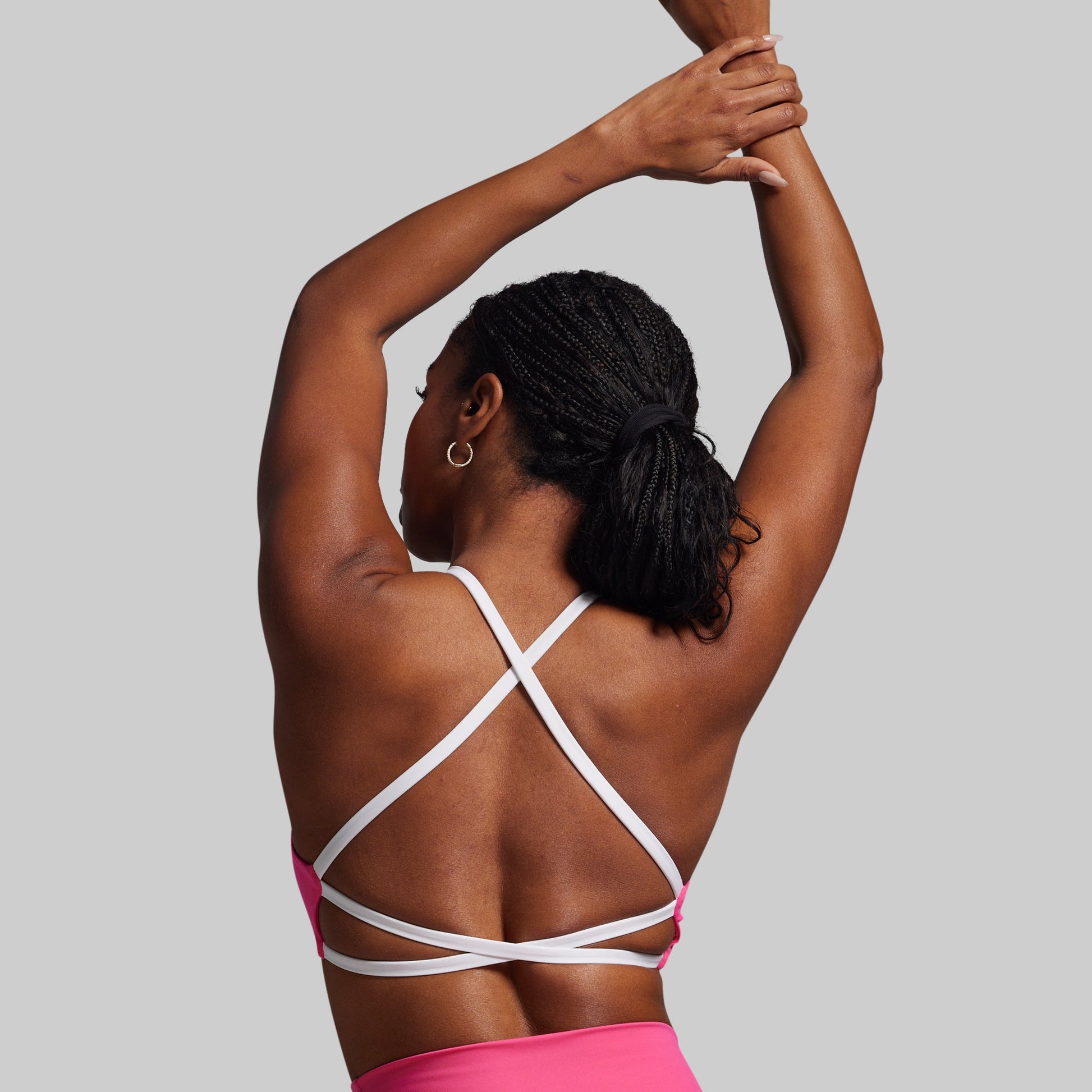 Person wearing a pink sports bra with white straps on a plain background