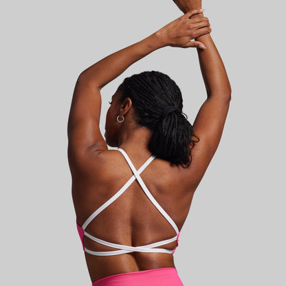 Person wearing a pink sports bra with white straps on a plain background