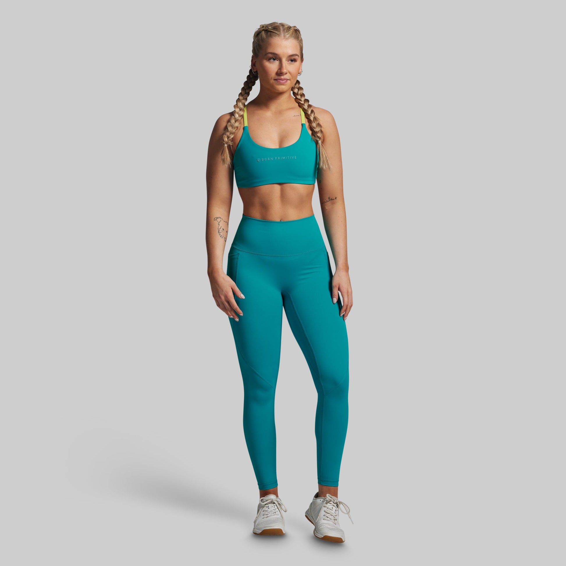 Woman wearing a teal sports bra and leggings set on a gray background