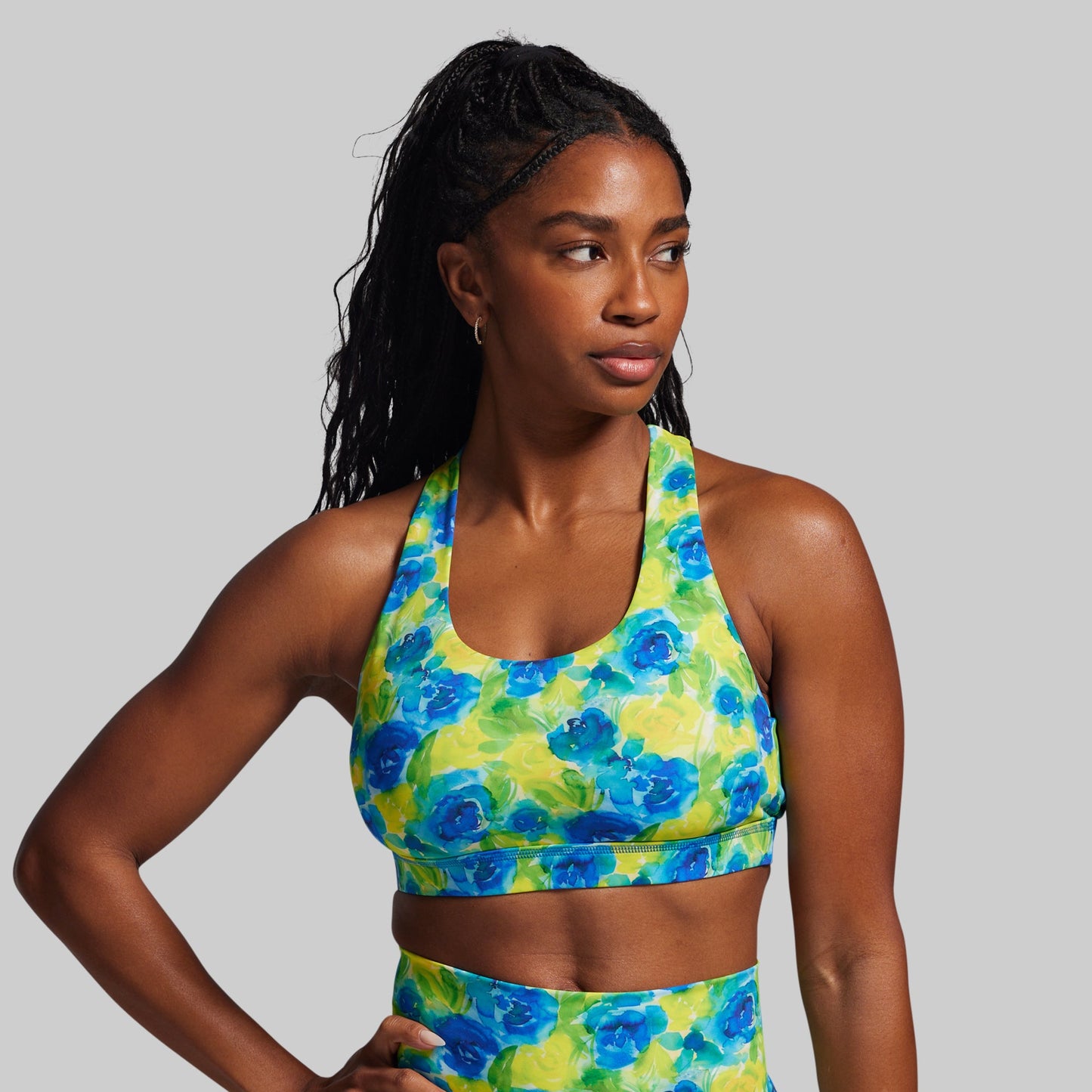 Woman wearing a colorful floral sports bra and leggings on a gray background