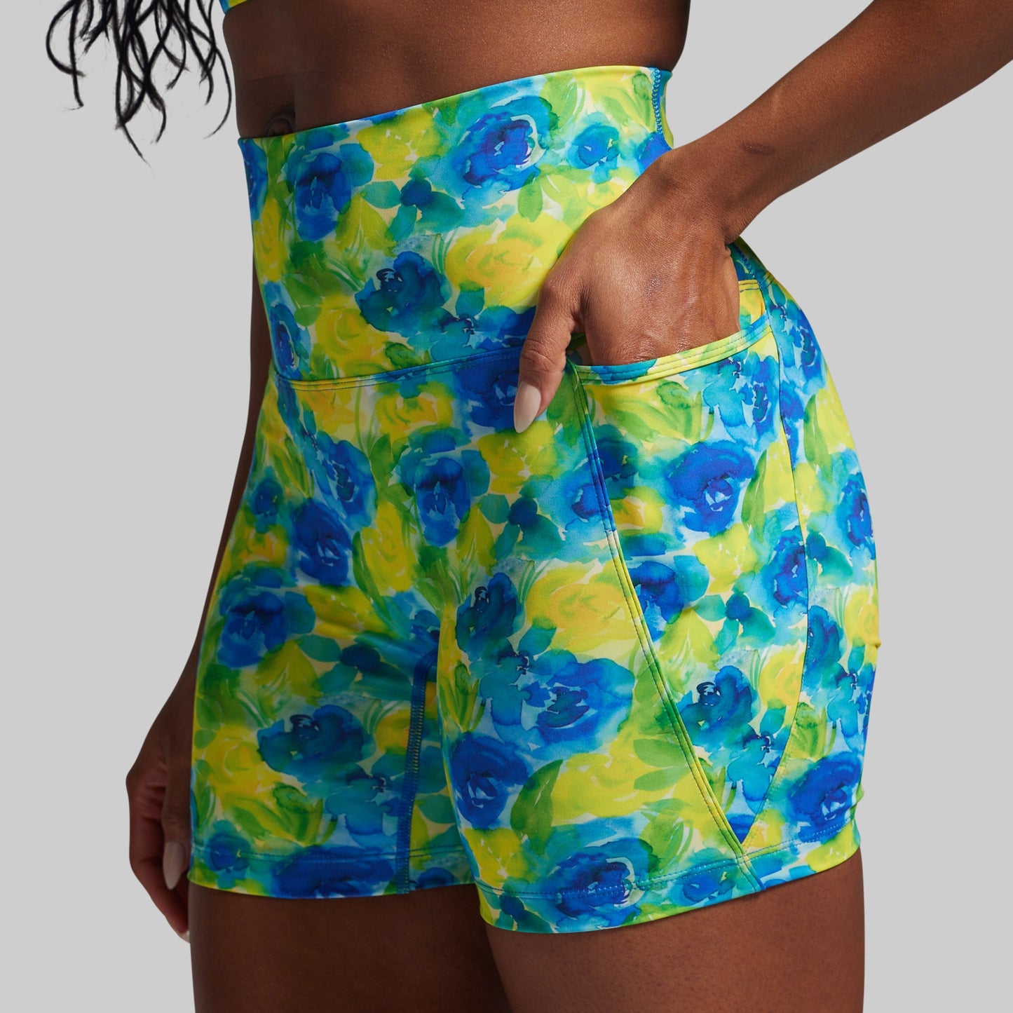 Person wearing colorful floral shorts with blue and green flowers on a gray background
